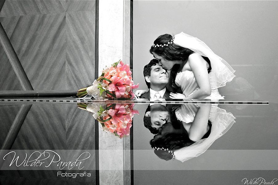 Novios en boda romántica en blanco y negro con ramo de flores en color, reflejo elegante en superficie, fotografía artística de matrimonio.