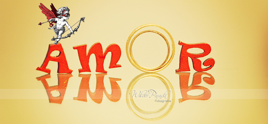 Fotografía conceptual de bodas que forma la palabra "Amor" utilizando letras rojas tridimensionales y una alianza de oro como la letra "O", con un cupido ilustrado sobre la letra "A" y un reflejo nítido sobre una superficie dorada brillante. Tienes Preguntas sobre Fotos de Boda