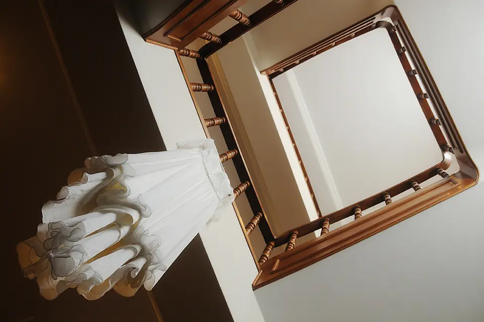 Vestido de novia blanco colgado en el pasamanos de una escalera de madera, detalles del getting ready por Wilder Fotografía