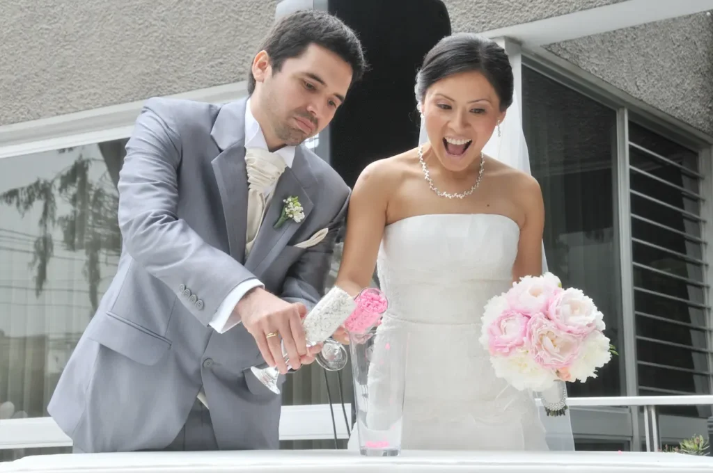 Novios vertiendo arena rosa y blanca en un frasco de cristal durante su ceremonia de boda.