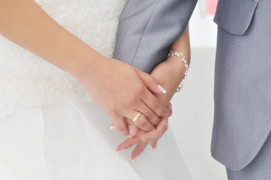 Detalle de las manos entrelazadas de los novios mostrando el anillo de bodas y pulsera de plata.