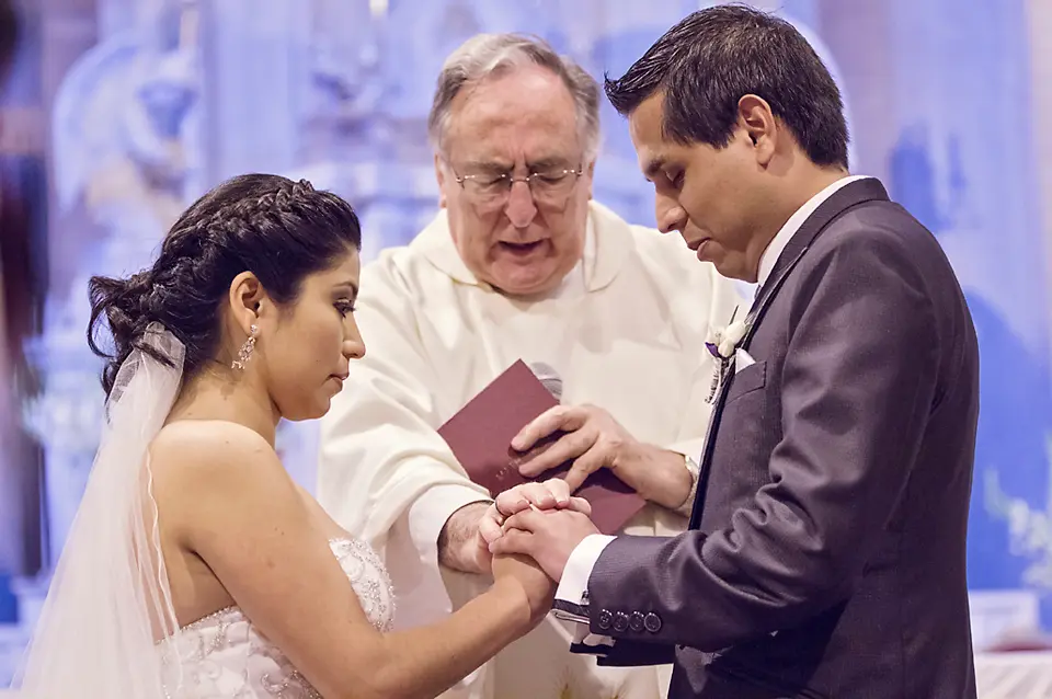 Primer plano del sacerdote bendiciendo la unión de los novios mientras ellos se toman de las manos durante el rito matrimonial.