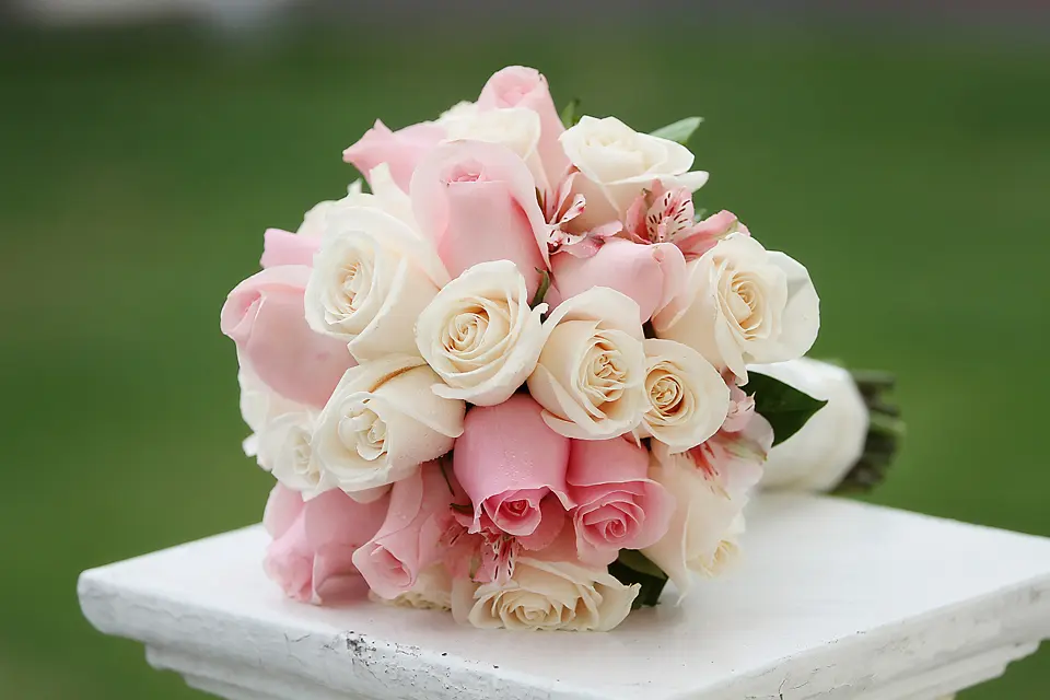 Ramo de novia con rosas rosadas y blancas sobre pedestal blanco, detalles de boda capturados por Wilder Fotografía en Chía.