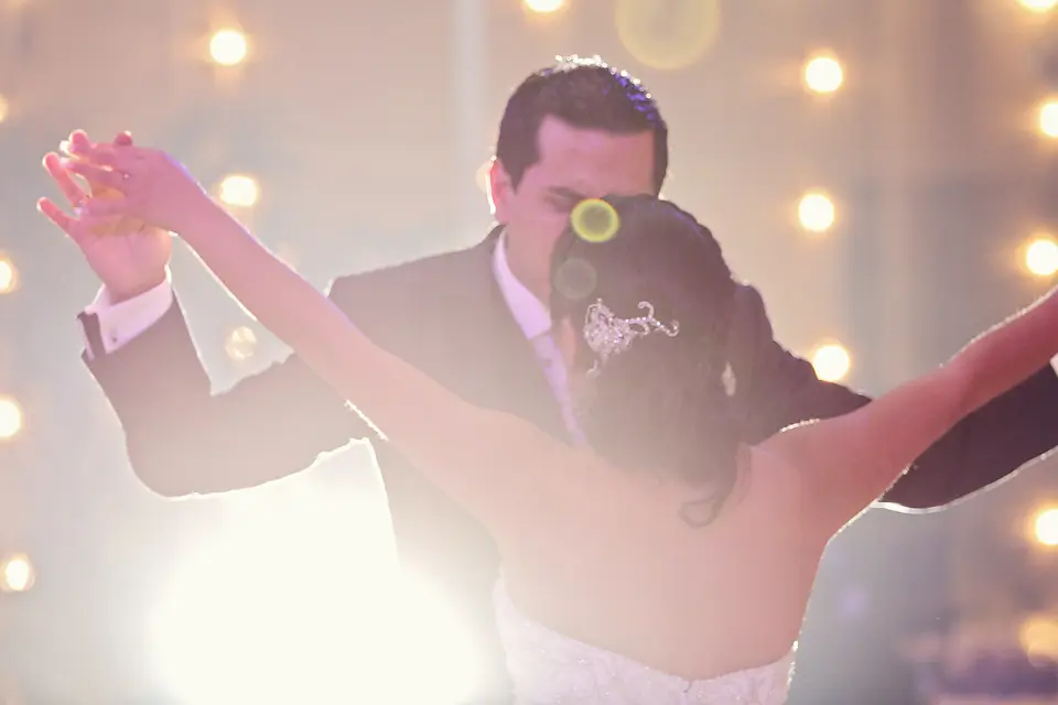 Los recién casados bailando abrazados en la recepción, con un efecto de luces cálidas de fondo y destellos románticos a contraluz.