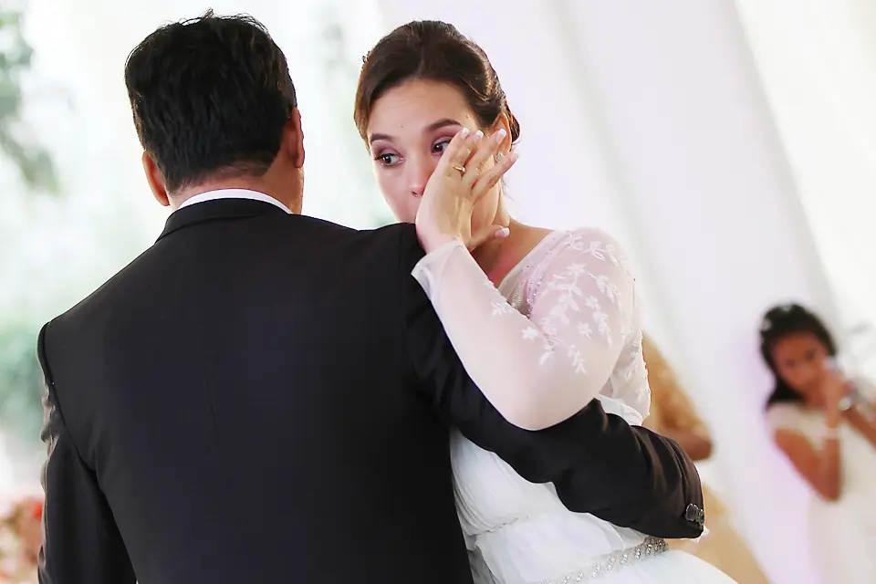 Primer plano de la novia secándose una lágrima de felicidad mientras baila abrazada al novio durante la celebración de bodas.