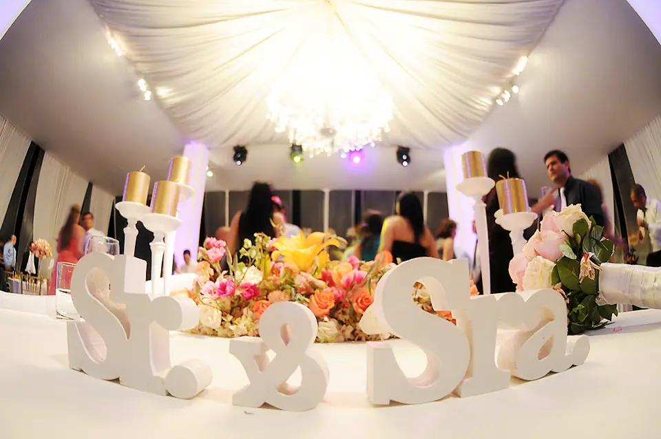 Letras decorativas de madera blanca con la inscripción Sr. y Sra. en la mesa principal de los novios, con arreglos florales y velas doradas.