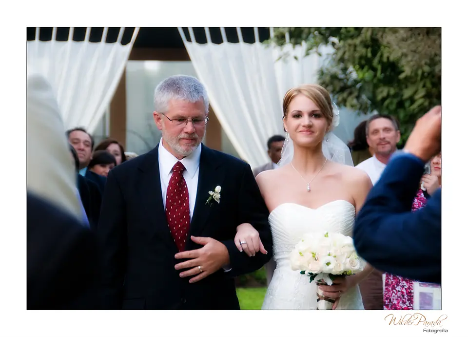 Primer plano de una novia sonriente del brazo de su padre momentos antes de iniciar su matrimonio en una zona verde de Cundinamarca.