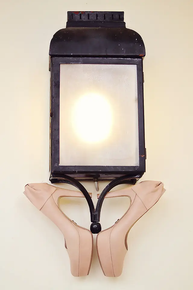 Zapatos de novia color nude colocados sobre un farol antiguo de pared iluminado, fotografía de detalles de boda en Chía.