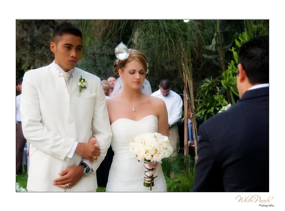 Pareja de novios escuchando los votos durante su boda campestre en Chía, resaltando el vestido de novia blanco y el traje de novio beige.