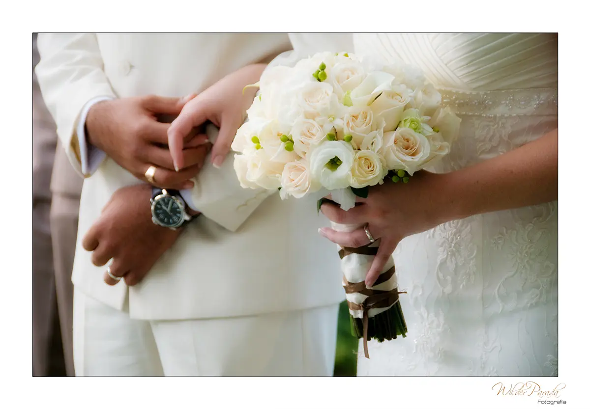 Foto detalle de las manos de los novios entrelazadas junto al ramo de rosas blancas en un matrimonio en la Sabana de Bogotá.