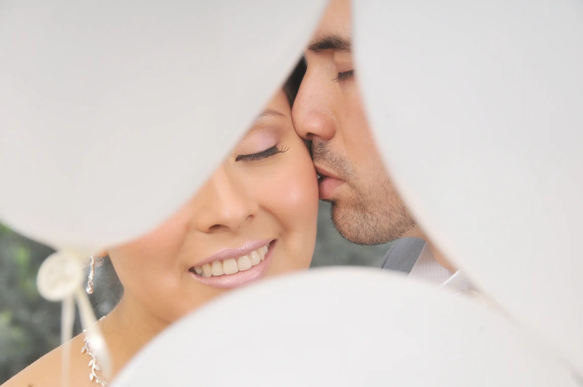 Primer plano extremo de un novio besando la mejilla de la novia, con globos blancos en primer plano creando un efecto de marco desenfocado en Chía
